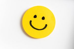 Drawing of a happy smiling emoticon on a yellow paper and white background.