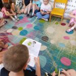 Odwiedziny uczniów ze szkoły podstawowej nr 4 w Lublińcu. Dzieci siedzą w kółku na podłodze i czytają książkę